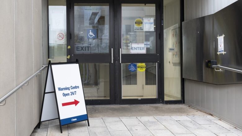 An arrow on a sign near a doorway shows the building is a warming centre open 24 hours, 7 days a week.