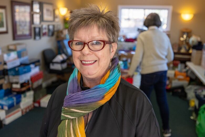 A woman wearing glasses and a brigh multicoloured scarf is seen smiling.