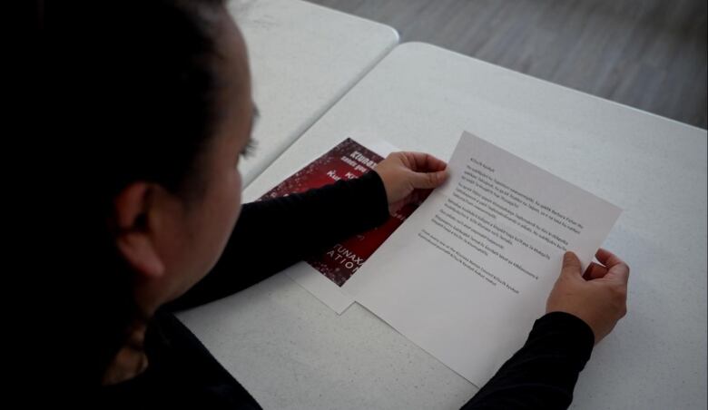 A woman holds a paper with words printed on it over a desk.