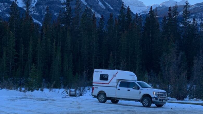 A camper van is pictured alone in a snowy, forested mountain landscape.