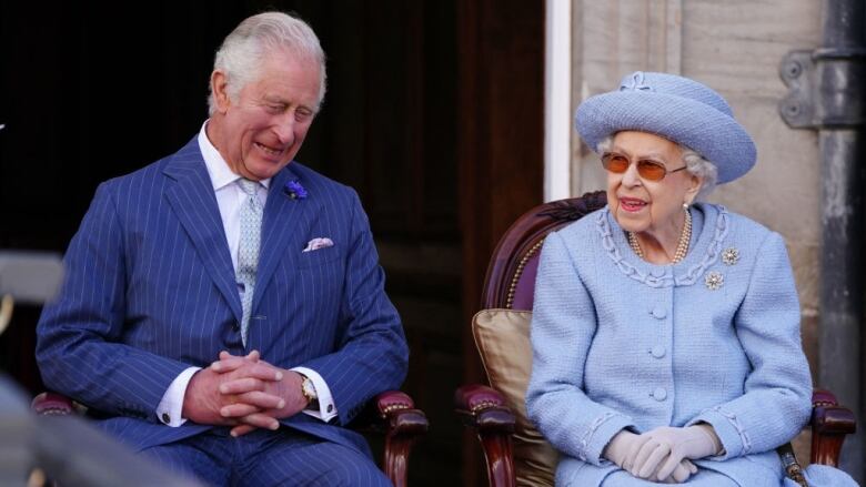 Two people sit in chairs in front of a large door.