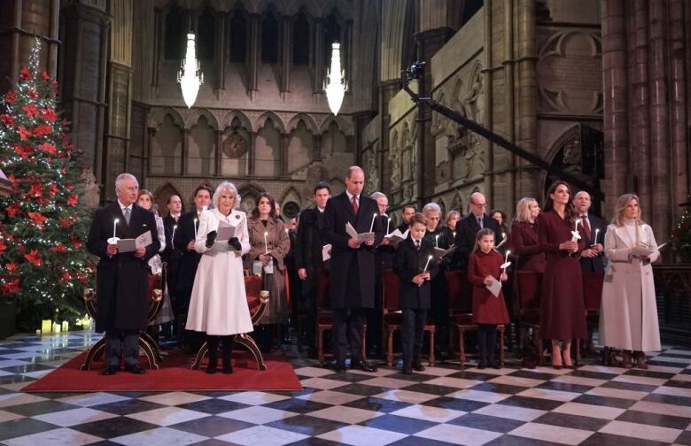 Several people stand singing in a large abbey.