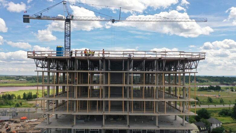 A crane looms over the concrete frame of a building with metal framing for windows visible on lower levels.