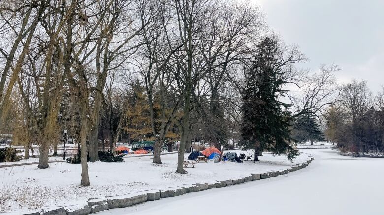 Park with snow on the ground and tents covered in orange and blue tarps.