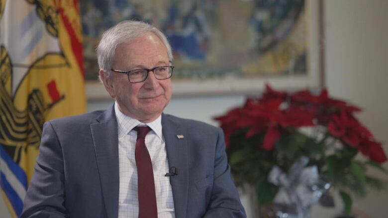 man in suit sitting in front of New Brunswick flag