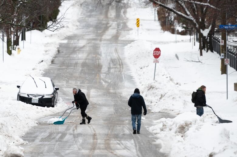 People clearing snow on a snowy street.