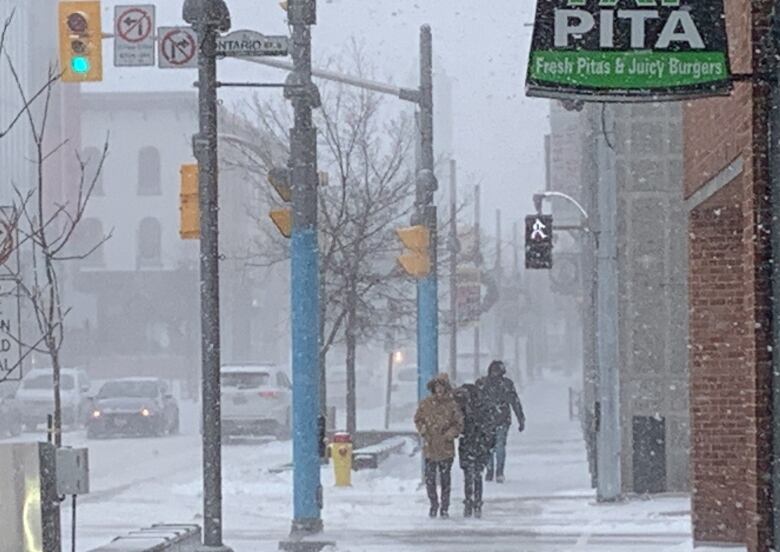 People are seen on the sidewalk with snow falling