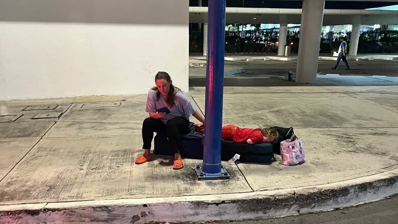 A woman sits outside an airport with a pile of luggage. 