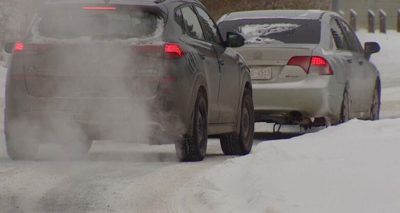 A grey SUV stopped just behind a white sedan on a snowy road.