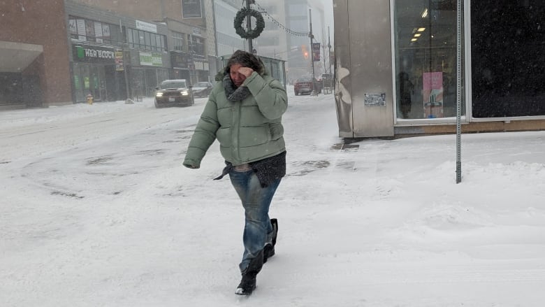 A woman in a puffy winter jacket shields her face from the wind