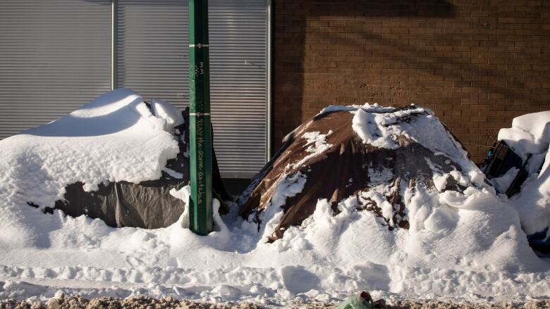 Two tents are pictured on a sidewalk, covered with snow.