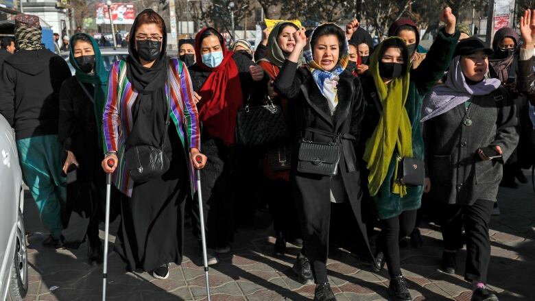 Women raise their fists and hold signs as they march along a street.