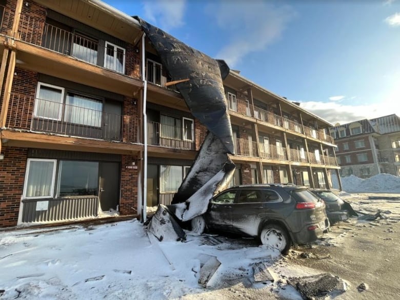 A tarp blown by strong winds partially covers an apartment building and a vehicle.