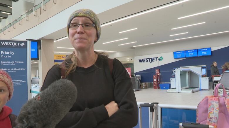 A woman standing with her arms crossed in front of the WestJet counter and the Calgary International Airport.