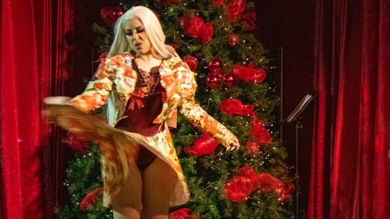 A drag performer dances in front of Christmas tree.