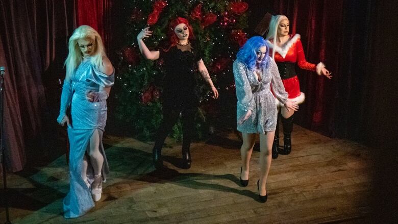 Drag performers dance in front of Christmas tree.