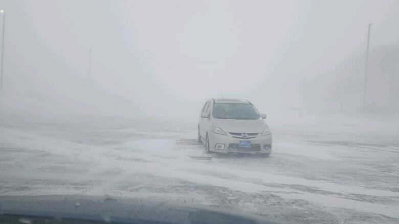 A vehicle is parked in a parking lot in heavy snow