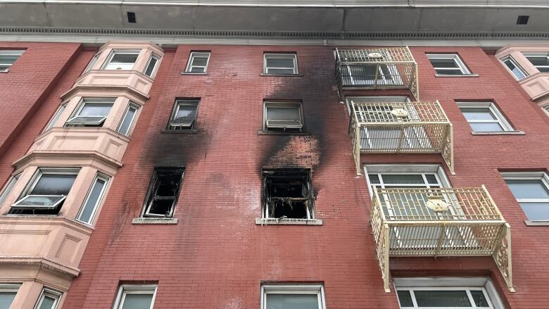 Charred windows, missing glass, on a red-brick apartment building.