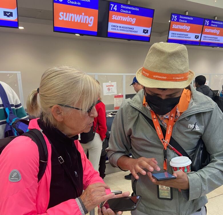 A woman speaks with a masked man taller than her with sunwing apparel.