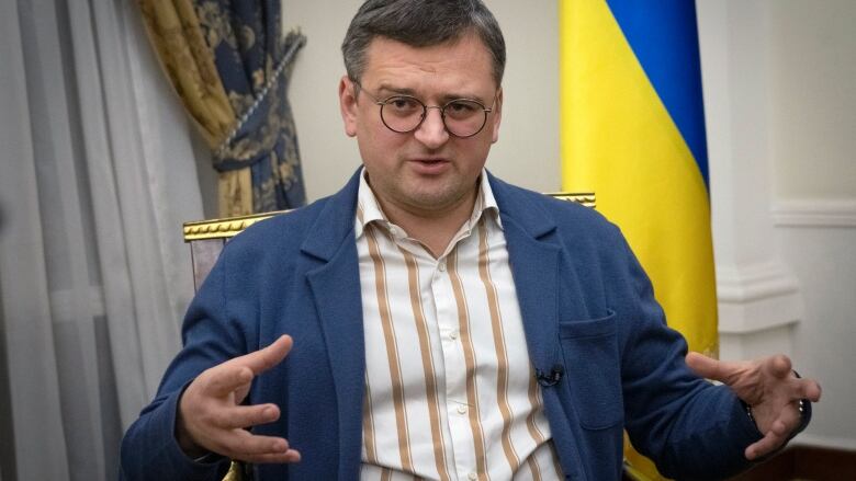 A man in a striped shirt and a blue jacket is seated.