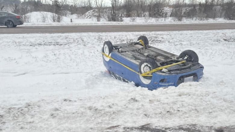 A blue car is flipped over in a median with yellow tape wrapped around its tires. 