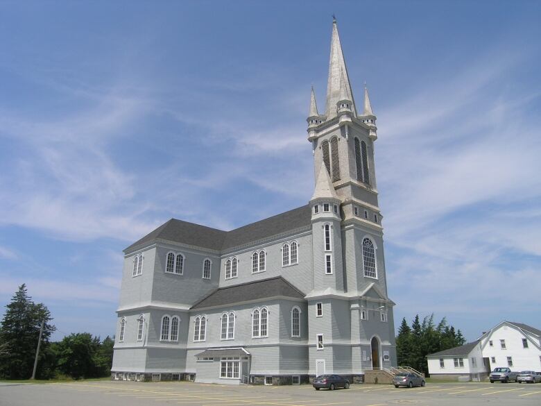 A grey wooden church is shown with the large tower on the right against a blue sky background in Digby County, Nova Scotia.