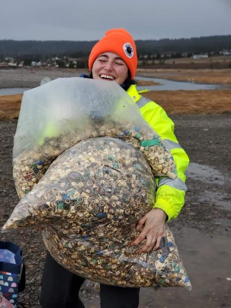 A woman stands on a beach holding plastic bags full of lobster bands