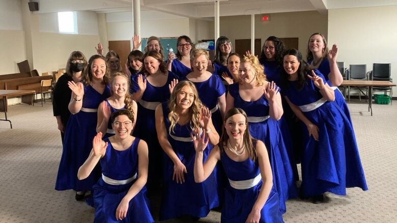 A group of women in blue dresses wave hands inside a room.