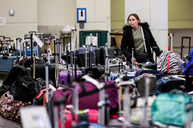 A person wearing a winter coat looks for her baggage in a pile of suitcases.