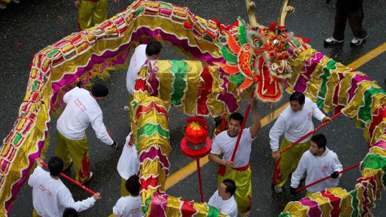 A group of men perform a dragon dance on the street, holding a giant puppet of dragon.