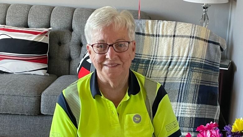 Woman in fluorescent green mail carrier uniform sits next to multi-coloured flowers in a vase. 