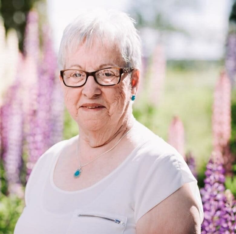 A woman in a white top poses in a portrait shot in front of a blurred background of lupins.