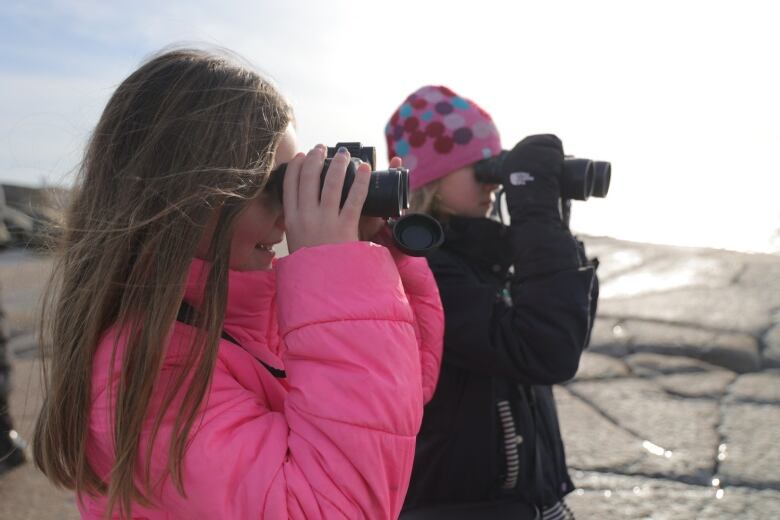 Two young girls look toward the ocean with binoculars