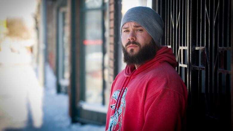 A man with a beard in a red sweater and grey toque stands outside.