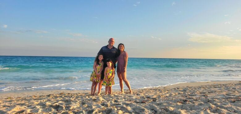 A man and woman and their two daughters stand at the beach with waves behind them.