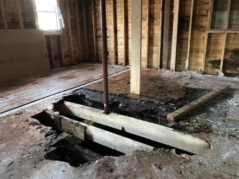 A room with a large hole in the floor and walls stripped to their beams as part of a renovation project.