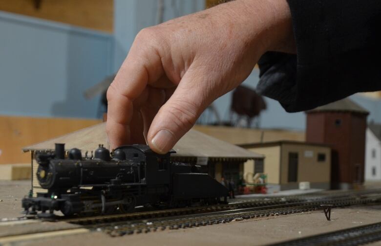 A small model of a black steam locomotive is placed on a section of model railway track by a hand.