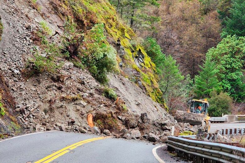 Heavy machinery removes debris from a road following a rock slide.