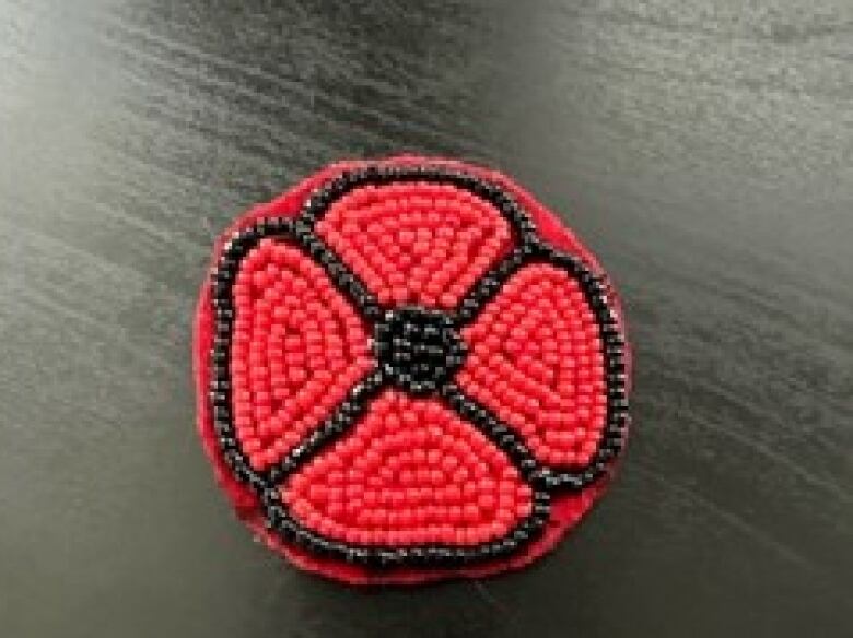 A beaded poppy is pictured on a black background.