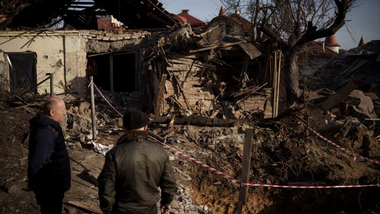 Two men stand before a destroyed home in Kyiv.