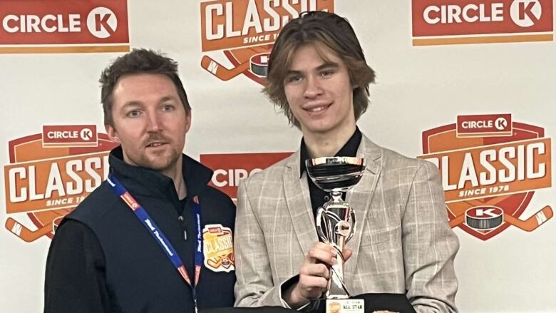 A smiling teenager holds a trophy, standing beside another man and in front of a banner reading Circle K Classic.