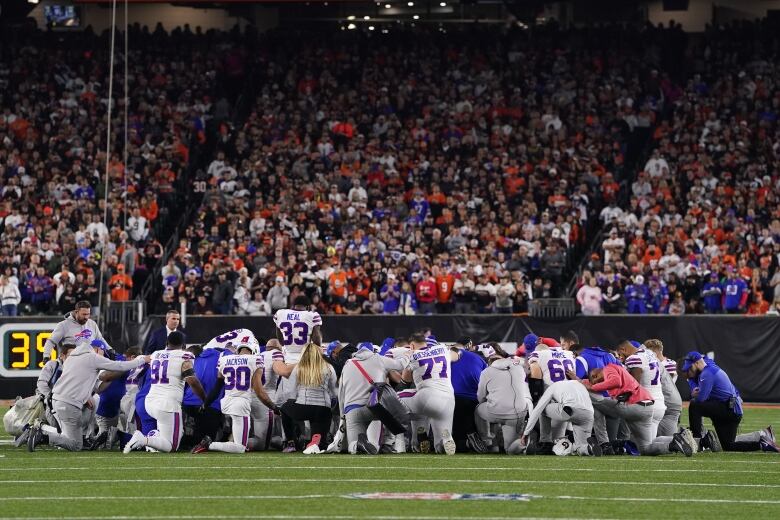 Buffalo Bills players are seen kneeling and praying in a football field as the audience watches at the back.