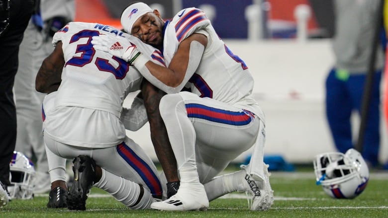 Neal has his back to the camera and is down on one knee. Hines is facing the camera and is also on one knee, while resting his hand on Neal's back and resting his head on his shoulder. His eyes are closed. They are both wearing their teams white uniforms, but their helmets are off.