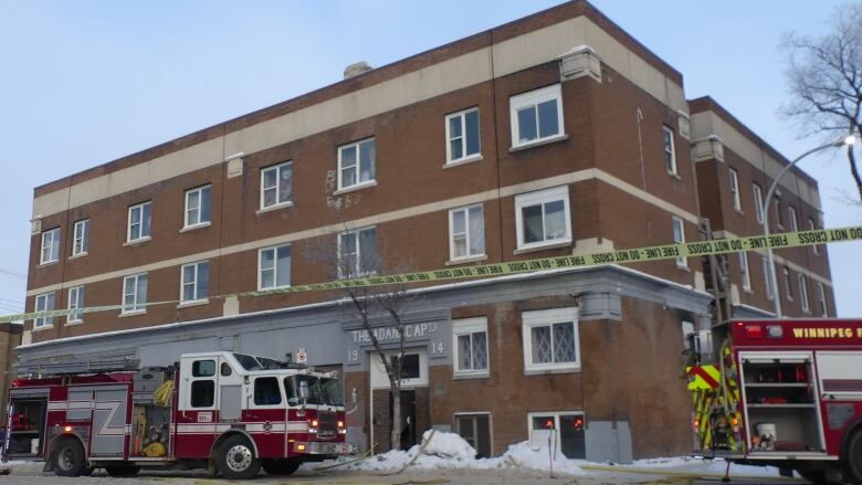 Fire trucks are seen outside of a red brick building surrounded by snow. 