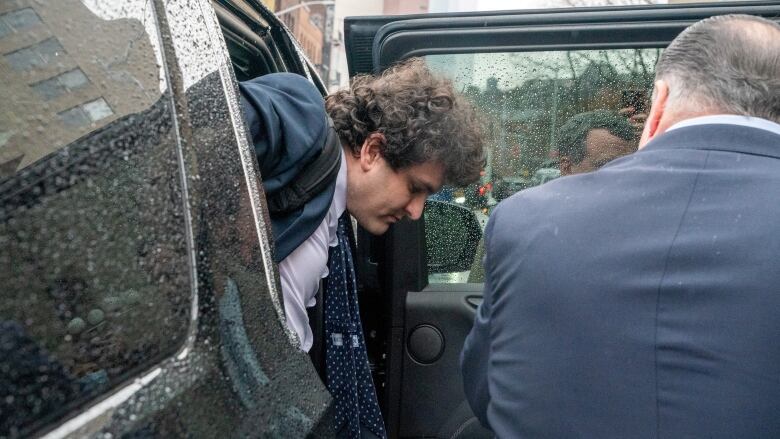 A man with curly hair exits a black car.