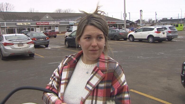 A woman stands in a parking lot holding a baby carrier. 