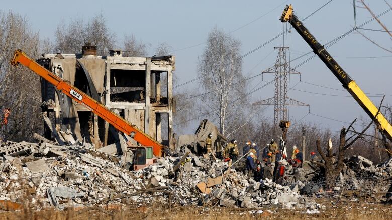 People and heavy machinery remove debris from a destroyed building.