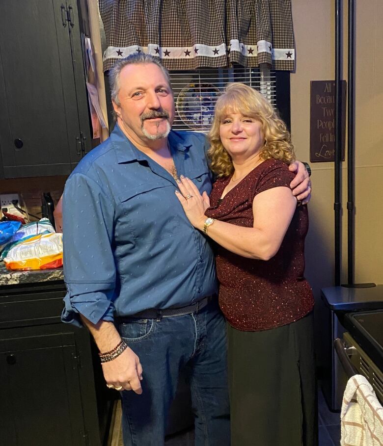 A husband and wife are seen standing in their kitchen, smiling.