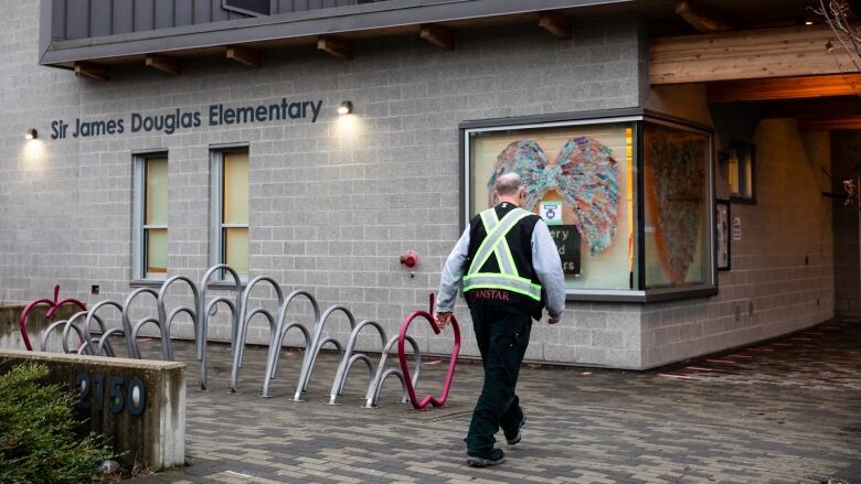 A man wearing a high visibility vest walks toward the entrance of Sir James Douglas Elementary School.