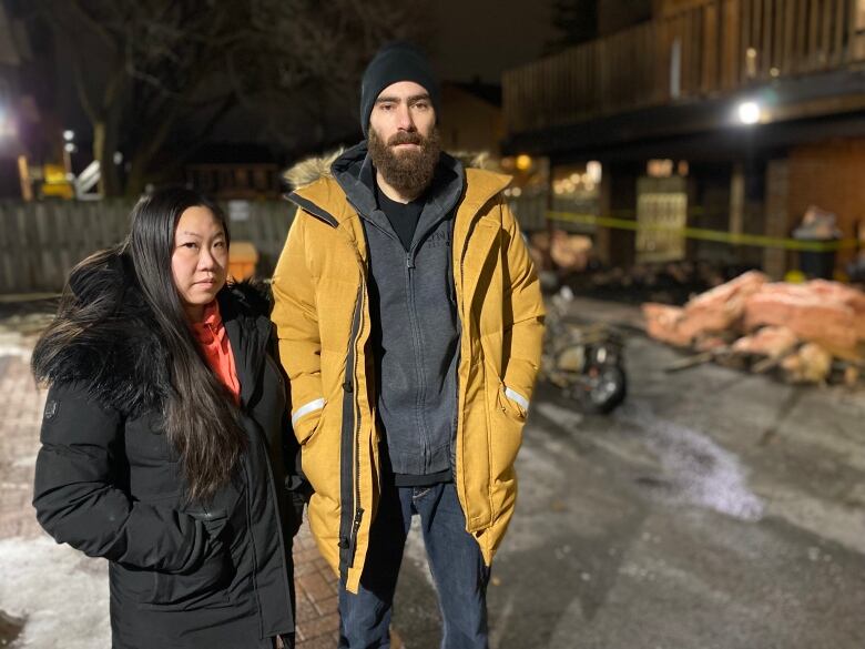 A woman and man stand in front of burned e-bikes and a pile of house insulation.